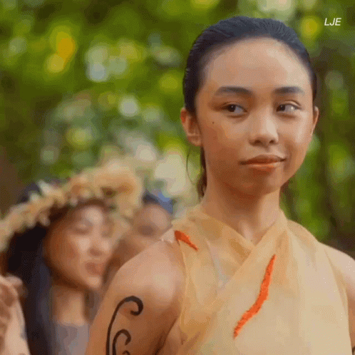 A Woman With A Tattoo On Her Arm Looks At The Camera With The Letters Lje Visible In The Corner GIF