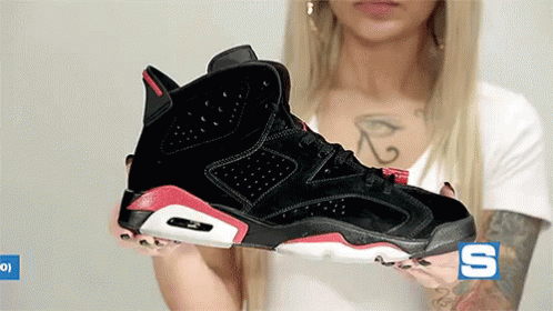 A Woman With A Tattoo On Her Chest Is Holding A Pair Of Black And Red Sneakers .. GIF