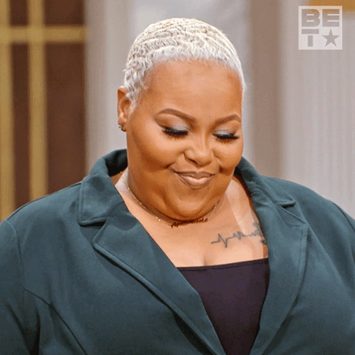 A Woman With A Tattoo On Her Chest Is Smiling In Front Of A Sign That Says Be Tv GIF