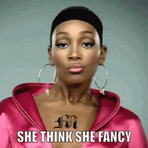 A Woman With A Tattoo On Her Chest Is Wearing A Pink Jacket And Hoop Earrings And Says She Think She Fancy GIF