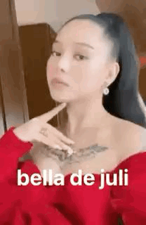 A Woman With A Tattoo On Her Chest Is Wearing A Red Dress And Holding Her Hand To Her Chin . GIF