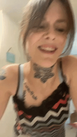 A Woman With A Tattoo On Her Neck Is Smiling And Looking At The Camera GIF