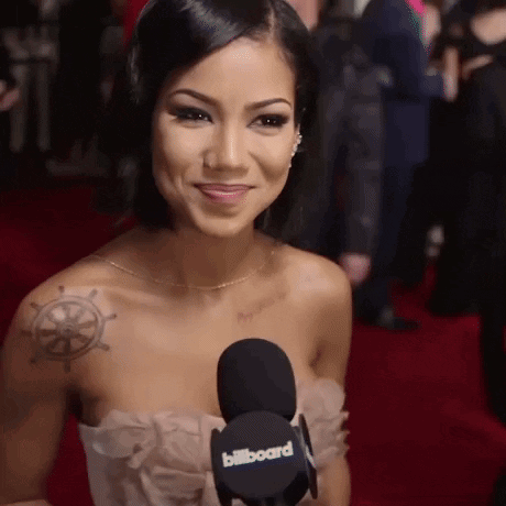 A Woman With A Tattoo On Her Shoulder Is Smiling And Holding A Billboard Microphone GIF