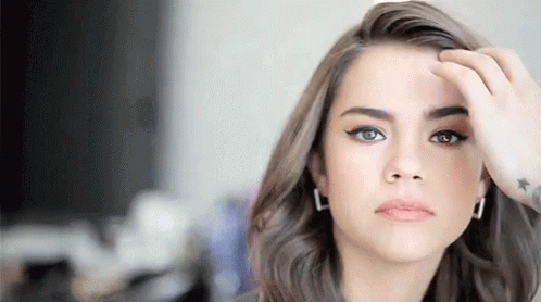 A Woman With A Tattoo On Her Wrist Is Touching Her Hair And Looking At The Camera . GIF