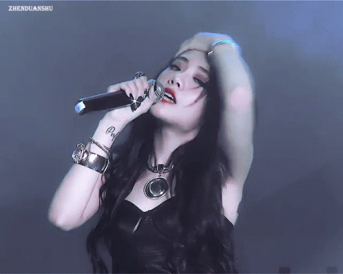 A Woman With A Tattoo On Her Wrist Singing Into A Microphone With Zhenguanshu Written On The Bottom Right GIF