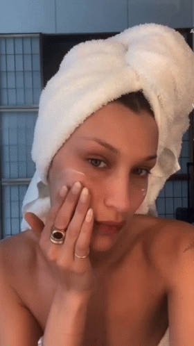 A Woman With A Towel Wrapped Around Her Head Is Applying A Cream To Her Face GIF