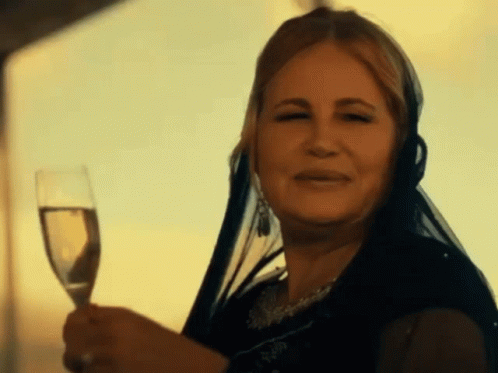 A Woman With A Veil On Her Head Is Holding A Glass Of Wine GIF