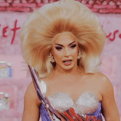 A Woman With A Very Large Blonde Wig And A Purple Dress GIF