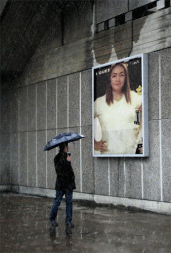 A Woman With An Umbrella Stands In Front Of A Billboard That Says I Guess GIF