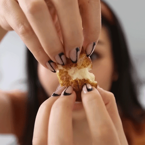 A Woman With Black And White Nails Holds A Piece Of Food In Her Hands GIF