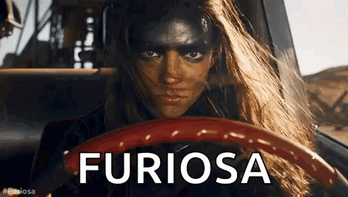 A Woman With Black Paint On Her Face Is Driving A Car And The Word Furiosa Is On The Steering Wheel . GIF