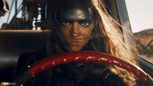 A Woman With Black Paint On Her Face Is Driving A Car With The Hashtag #Furiousa GIF