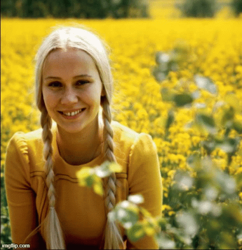 A Woman With Blonde Braids Is Smiling In A Field Of Yellow Flowers .. GIF