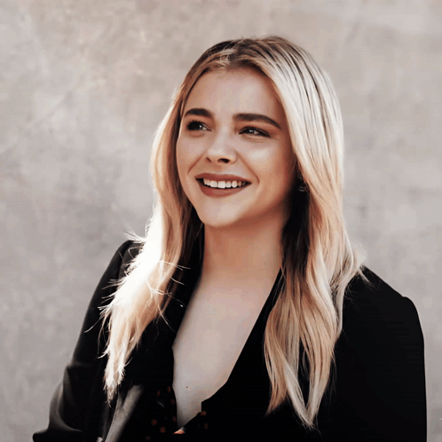 A Woman With Blonde Hair And A Black Jacket Smiles GIF