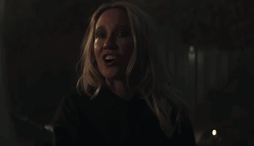 A Woman With Blonde Hair And A Black Shirt Smiles In The Dark GIF