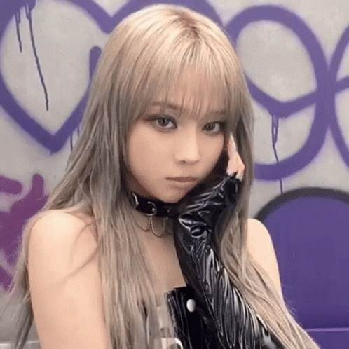 A Woman With Blonde Hair And A Choker On Her Neck Is Standing In Front Of A Purple Wall . GIF