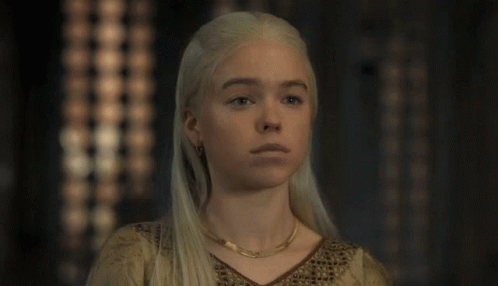 A Woman With Blonde Hair And A Gold Necklace Looks At The Camera GIF