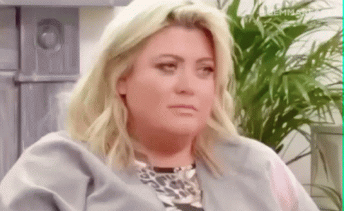 a woman with blonde hair and a leopard print shirt is sitting in front of a plant .