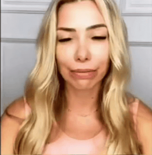 A Woman With Blonde Hair And A Pink Shirt Is Making A Funny Face . GIF