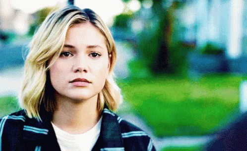 A Woman With Blonde Hair And A Plaid Jacket Is Looking At The Camera GIF