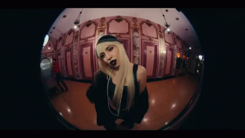 A Woman With Blonde Hair And Black Lipstick Is Standing In A Hallway . GIF