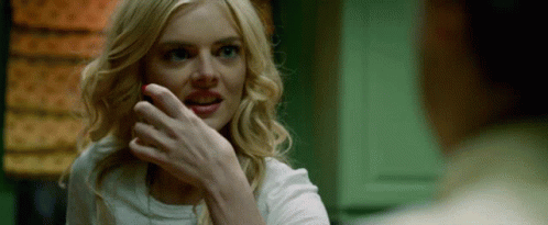 A Woman With Blonde Hair And Blue Eyes Is Smiling While A Man Holds Her Hand To Her Face . GIF