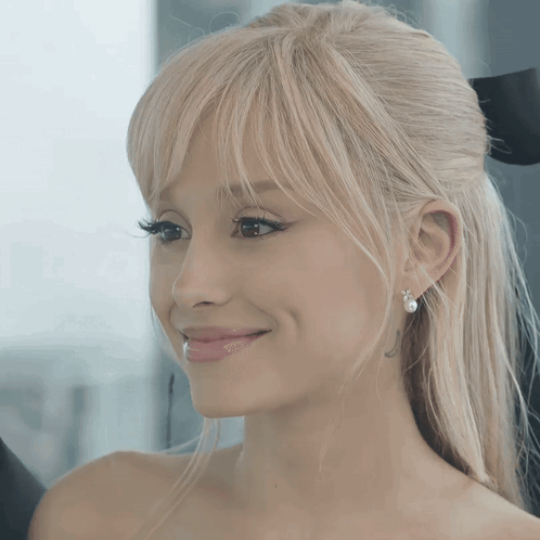 A Woman With Blonde Hair And Pearl Earrings Smiles For The Camera GIF