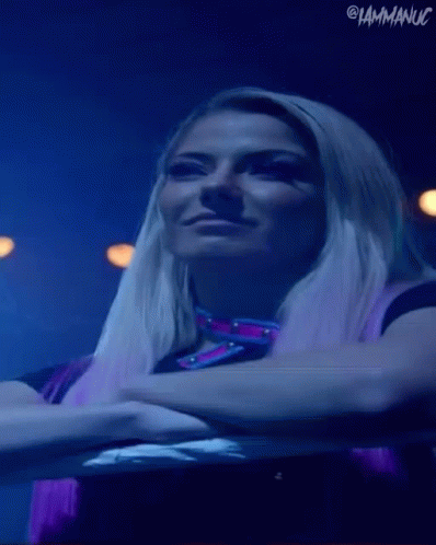 A Woman With Blonde Hair And Purple Hair Is Standing In A Dark Room With Her Arms Crossed . GIF