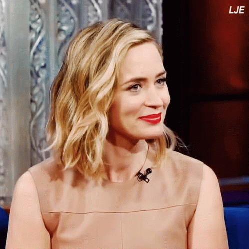 A Woman With Blonde Hair And Red Lips Is Sitting In Front Of A Microphone With The Letters Lje Above Her Head GIF