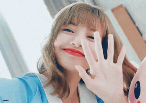 A Woman With Blonde Hair And Red Lips Is Waving Her Hand At The Camera . GIF