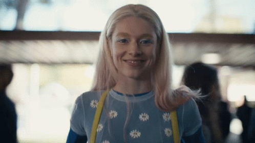 A Woman With Blonde Hair And White Eye Shadow Smiles For The Camera GIF