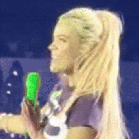 A Woman With Blonde Hair Is Holding A Green Object . GIF