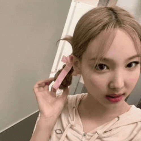 A Woman With Blonde Hair Is Holding A Pink Ribbon In Her Hair . GIF