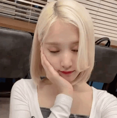 A Woman With Blonde Hair Is Holding Her Hand To Her Face . GIF