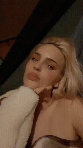 A Woman With Blonde Hair Is Laying Down With Her Hand On Her Chin GIF