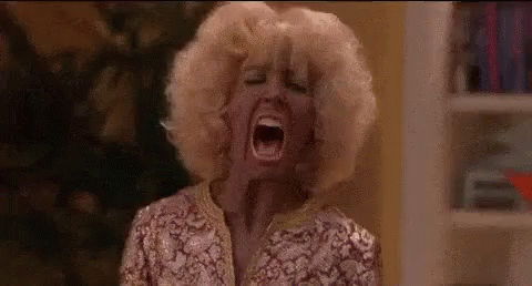 A Woman With Blonde Hair Is Screaming With Her Mouth Wide Open In A Room . GIF