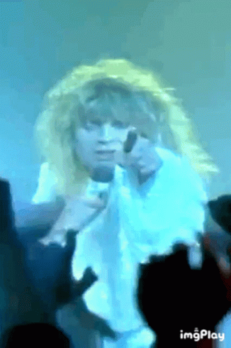 A Woman With Blonde Hair Is Singing Into A Microphone While A Crowd Watches . GIF