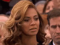 A Woman With Blonde Hair Is Sitting In A Crowd Of People . GIF