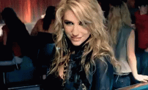 A Woman With Blonde Hair Is Sitting In A Dark Room Looking At The Camera GIF