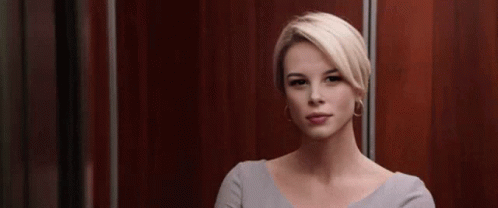 A Woman With Blonde Hair Is Sitting In An Elevator And Looking At The Camera . GIF