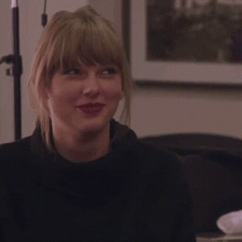 A Woman With Blonde Hair Is Smiling With Her Eyes Closed And Wearing A Black Sweater . GIF