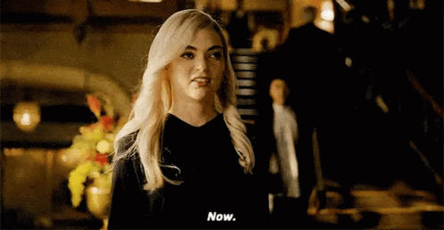 A Woman With Blonde Hair Is Standing In A Dark Room And Talking To A Man . GIF