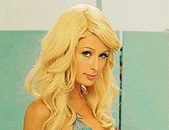 A Woman With Blonde Hair Is Standing In Front Of A Blue Wall . GIF