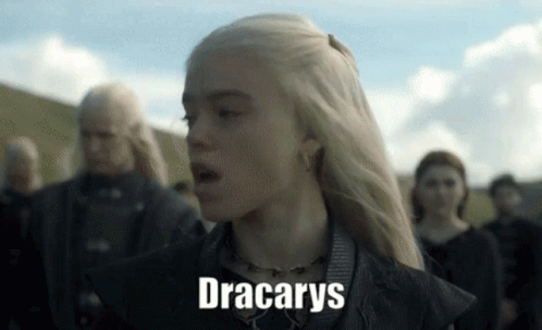 A Woman With Blonde Hair Is Standing In Front Of A Group Of People And The Word Dracarys Is On Her Face . GIF