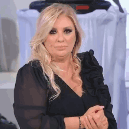 A Woman With Blonde Hair Is Wearing A Black Ruffled Top And A Black Bracelet On Her Wrist . GIF