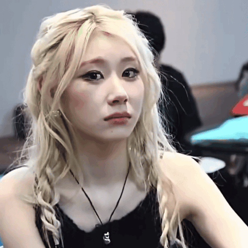 A Woman With Blonde Hair Is Wearing A Black Tank Top And A Black Necklace GIF