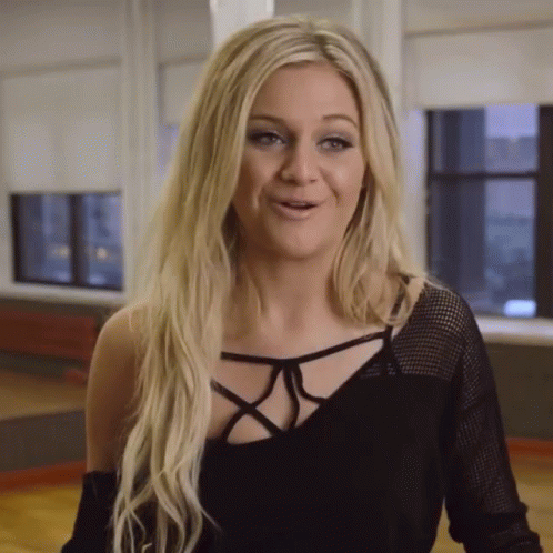 A Woman With Blonde Hair Is Wearing A Black Top And Smiling GIF