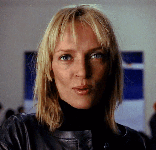 A Woman With Blonde Hair Is Wearing A Black Turtleneck And A Leather Jacket GIF