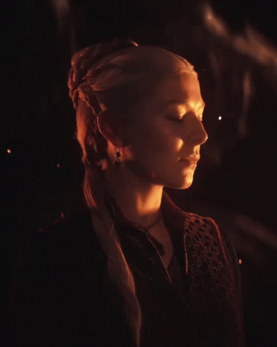 A Woman With Blonde Hair Is Wearing A Black Vest And A Necklace GIF