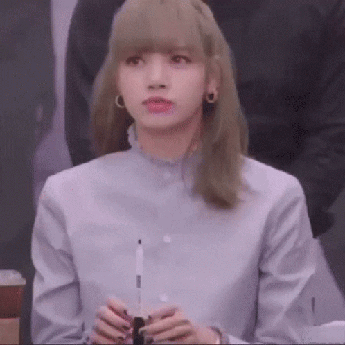 A Woman With Blonde Hair Is Wearing A Blue Shirt And Holding A Pen In Her Hands . GIF